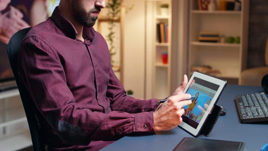 Male artist doing skin retouching on tablet computer using a pen at night time.