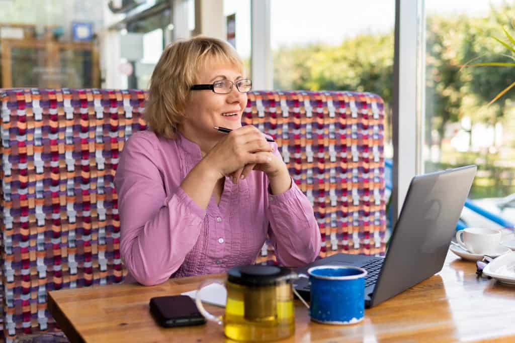 A woman with a laptop is working in an office. A middle-aged businesswoman is in a cafe. She smiles.